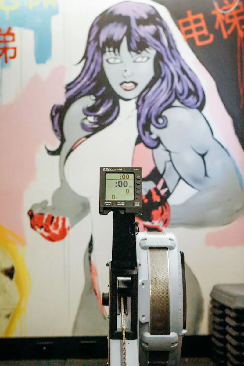 Rowing machine in front of a purple-haired heroine mural