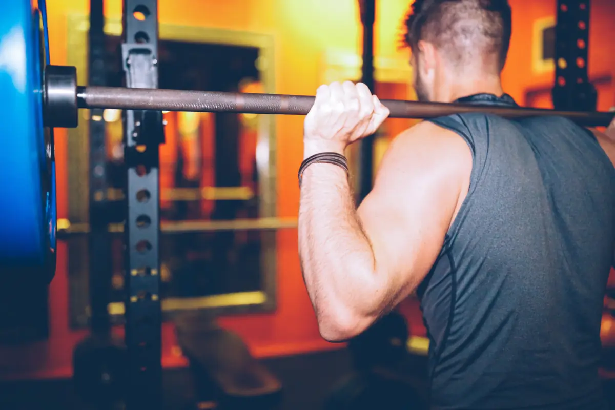 Member setting a loaded barbell on his back in the rack